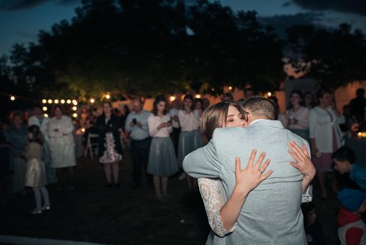 Bride and groom hugging at night on the background of guests at the banquet.
