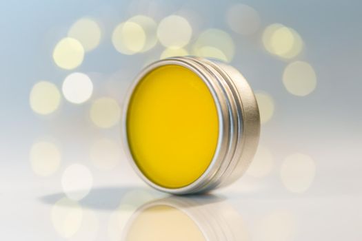 Lip balm in metal jar over sparkling light bokeh background. Empty label mock up. Natural cosmetic winter care product. Selective focus