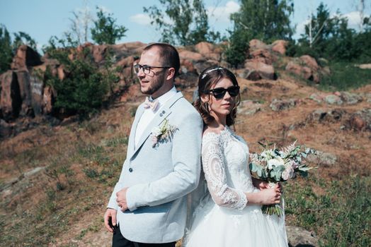 Wedding photography fashionable bride and groom in sunglasses on the nature on the rocks