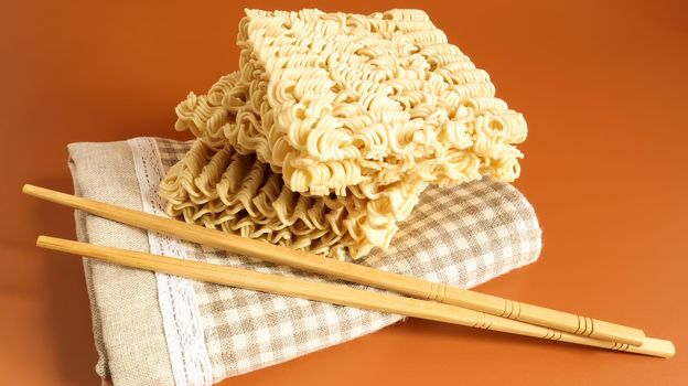 raw instant noodles on a towel with chopsticks on a yellow background. pasta, for the preparation of which it is enough to pour boiling water over it and wait a few minutes. Copy space