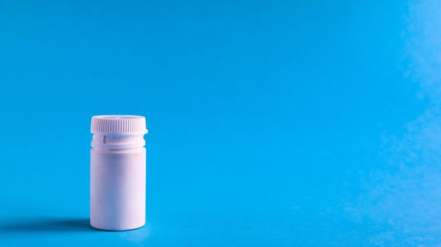 White pills and white plastic little bottle with copy space on dark blue background, concept of health and medicine. Copy space for your text. Healthcare concept. Medical social media blog template