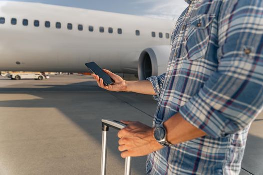 Cropped photo of male hand holding modern mobile phone with plane on the background