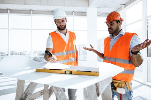 Two young engineers man looking at project plan on the table in construction site