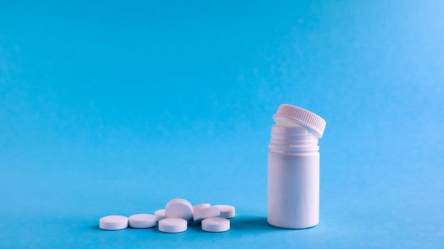 White pills and white plastic little bottle with copy space on dark blue background, concept of health and medicine. Copy space for your text. Healthcare concept. Medical social media blog template