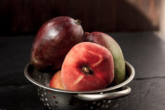 Mango and peach fruits in metal colander.