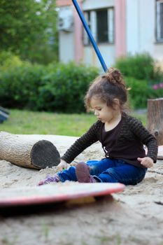 Little kid girl playing in a children sandbox