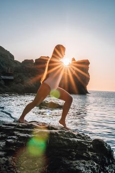 Young woman in swimsuit with long hair practicing stretching outdoors on yoga mat by the sea on a sunny day. Women's yoga fitness pilates routine. Healthy lifestyle, harmony and meditation concept.