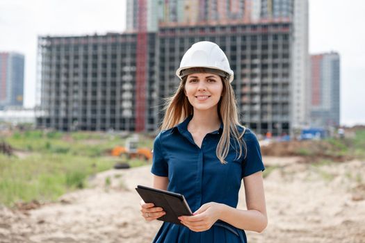 Female construction engineer. Architect with a tablet computer at a construction site. Young Woman look in camera, building site place on background. Construction concept.