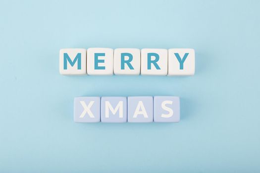 Merry Xmas minimal concept in light pastel blue colors. Handwritten text Merry Christmas on blue tablet against blue background. Modern trendy Merry Xmas concept