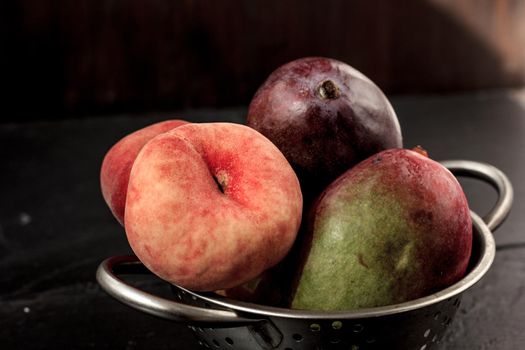 Mango and peach fruits in metal colander.