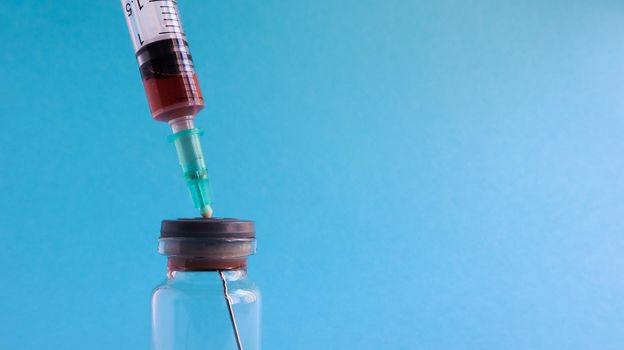 Coronavirus flu and pandemic vaccines, syringe and vial with red liquid on a blue background. medical concept, subcutaneous injection, treatment of the disease. Copy space for text or logo.