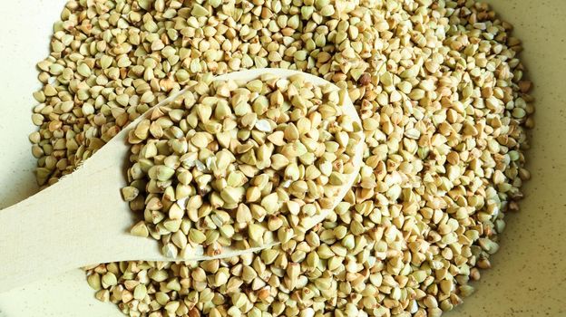 Uncooked green buckwheat in a beige plate with a wooden spoon. Great food. healthy groats. Organic raw non-fried vegetarian food. The concept of a healthy and balanced diet. Dietary foods