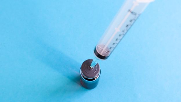 A syringe sticks out of a red liquid bottle. Isolated on a blue background. Medicine, injections, vaccines and disposable syringes, drug concept. Sterile bottle. Glass ampoule medical for injection