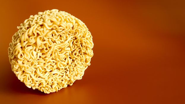 Korean instant noodles in the shape of a circle on a brown background. A yellowish-white dried raw vermicelli with long round lines and twisted in different directions into a briquette