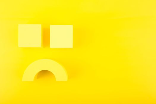 Creative flat lay with unhappy, sad smile symbol made of yellow figures on yellow background with copy space. Concept of emotions, emoji, mental health or unsatisfied customer