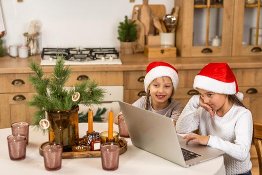 Two little girls watching online school while sitting at table dining room table.