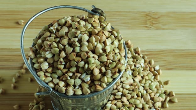 Small metal bucket with raw buckwheat on a board on a brown background. Organic vegetarian food. The concept of a healthy and balanced diet. Dietary nutrition. Copy space. Top view