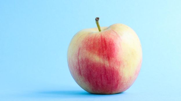 One beautiful, appetizing and fresh apple on a blue background. Healthy sweet food concept