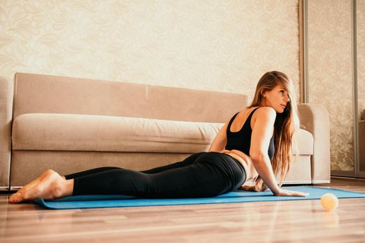 Young woman with long hair, fitness instructor in black sportswear, doing stretching and pilates on yoga mat at home. Female fitness yoga routine concept. Healthy lifestyle harmony and meditation