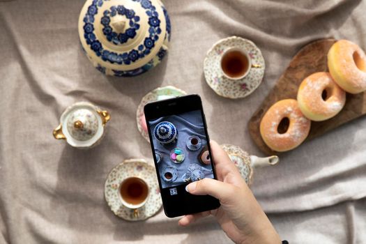 Top view picture of lady,blogger sitting in cafe and making photo with mobile of food, afternoon tea with doughnuts and macarons on the table high angle, food and social media concept close up