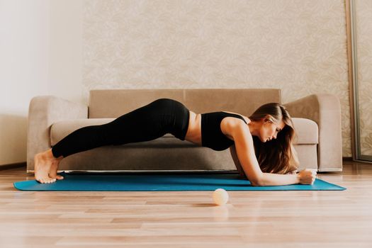 Young woman with long hair, fitness instructor in black sportswear, doing stretching and pilates on yoga mat at home. Female fitness yoga routine concept. Healthy lifestyle harmony and meditation