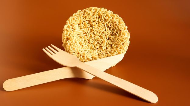 Raw instant noodles in the shape of a circle with a wooden disposable fork. pasta, for the preparation of which it is enough to pour boiling water and wait a few minutes. spaghetti. Copy space.