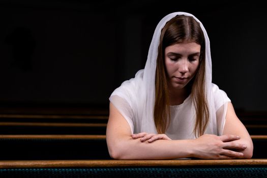 A young modest girl with a handkerchief on her head is sitting in church and praying. The concept of religion, prayer, worship.