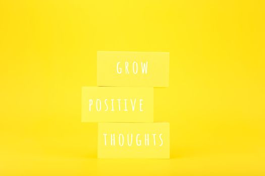 Positive affirmation, mental health or quote concept. Grow positive thoughts written on stack of yellow rectangles on yellow background. Motivational text for inner piece and happiness