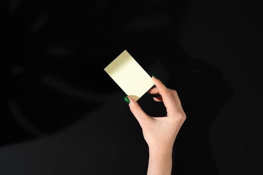 Female hand holding blank businesscard. Creative photo with shadow close up