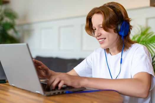 Red-haired teenager during an online video call with friends and smiling. Modern technologies and youth culture concept.