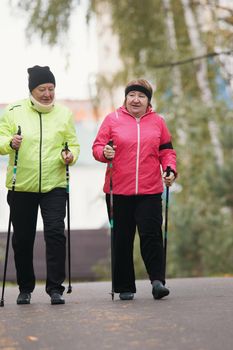 Old women walking on sidewalk in an autumn park during a scandinavian walk. Wide shot