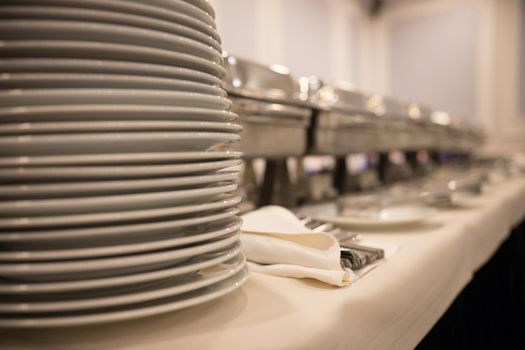 Ceramic white plates stand on top of each other on a table on the trays background. Close up