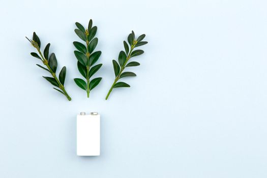 Eco energy or green power illustration with a white battery and sprigs leaves on a light background with copy space for text