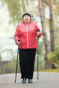 One elderly woman is doing Scandinavian walking in the park. Mid shot