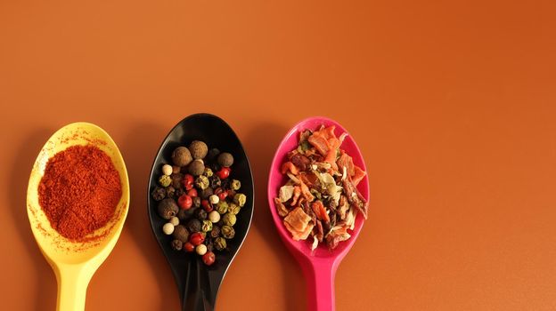 Various spices in plastic spoons on a brown background. Copy space. A mixture of peppers, red smoked paprika, seasoning twelve vegetables