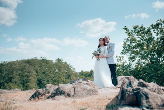 Wedding photo of the bride and groom in a gray-pink color on nature in the forest and rocks