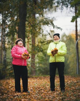 Mature woman throwing leaves into the air in an autumn park. Wide shot