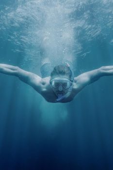 Young man in mask with snorkel diving underwater in blue sea.