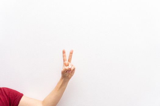 Left hand of white caucasian woman or girl makes peace gesture or victory gesture with two fingers, white background, body language concept. copyspace.