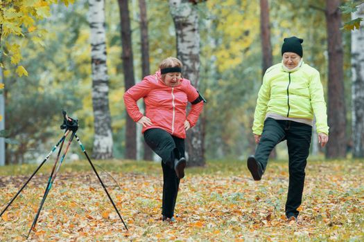 Mature woman performing a leg warm-up in an autumn park after a scandinavian walk. Wide shot