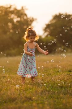 Pretty girl runs for the bubbles in the park on the sunset