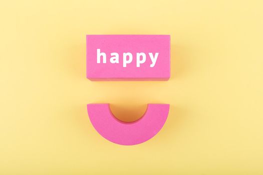 Creative flat lay with pink happy smile symbol made of toy figures on bright yellow background. Concept of Smile day, emotions, emoji or mental health