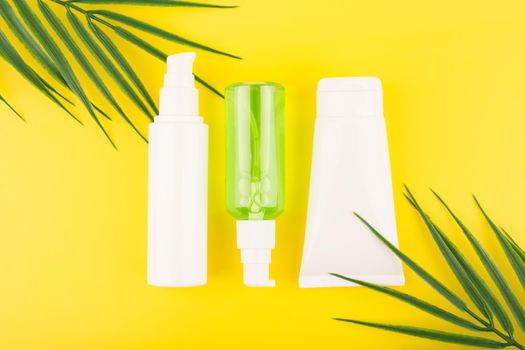 Trendy colorful composition with set of cosmetic tubes with beauty products on yellow background with palm leaves. Concept of creams with fruit extracts or skin products with sunblock