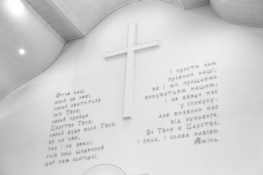 Bible theme. Prayer Our Father in Ukrainian on a white wall with a large cross