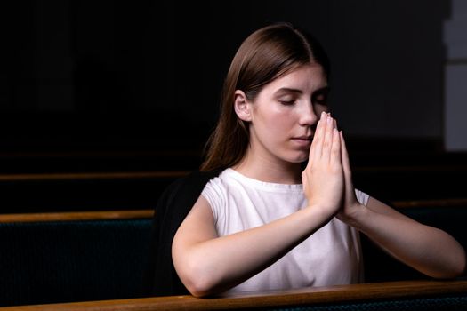 A Christian girl in white shirt is sitting and praying with humble heart in the church.