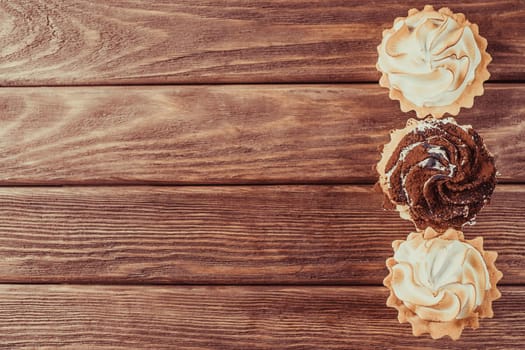 Three holiday cupcakes with cream on a wooden background, top view. Copy-space in left part of image.