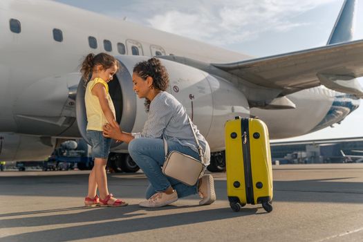 Mom and daughter with a yellow suitcase near the plane before takeoff. Trip concept