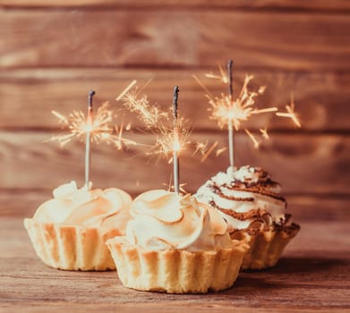 Three holiday cupcakes with sparklers on a wooden background.