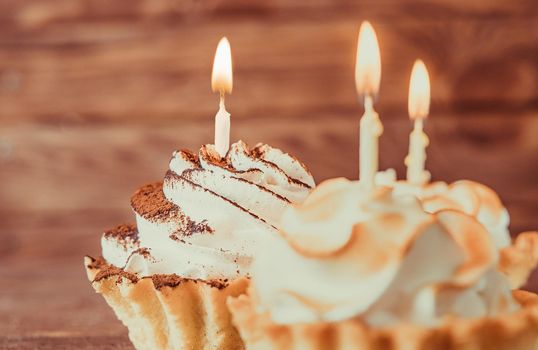 Birthday holiday sweet cupcakes with burning candles on a wooden background, close-up.