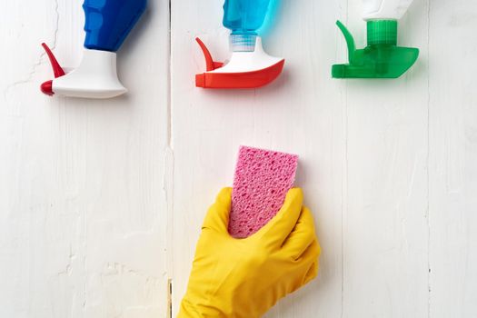 Hand in glove with cleaning supplies above white wooden background, top view